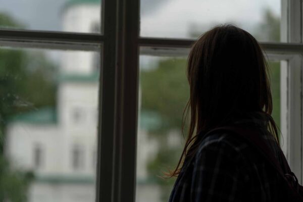 Close,Up,Of,Young,Woman,Looking,Out,Window,In,Unlit