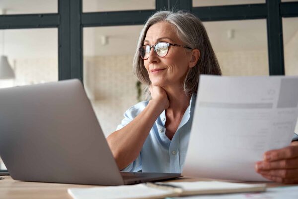 Middle aged woman using laptop and sitting at a desk.