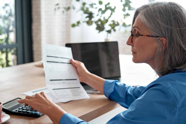 Senior,Mature,Business,Woman,Holding,Paper,Bill,Using,Calculator,,Old