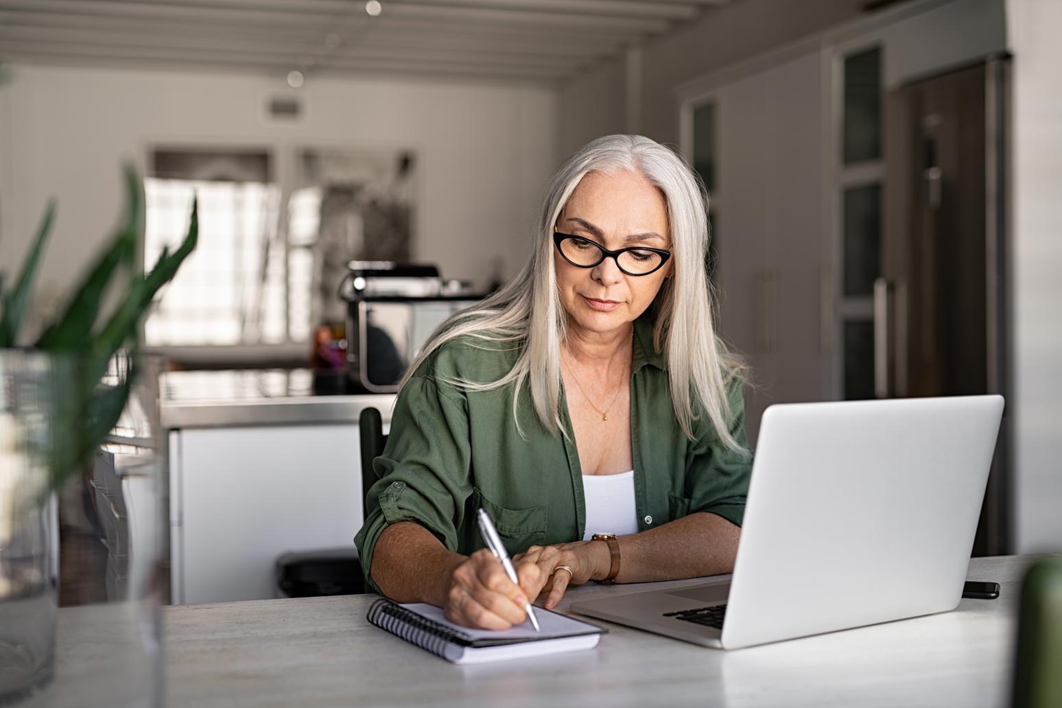 woman taking notes in notebook while using laptop at home