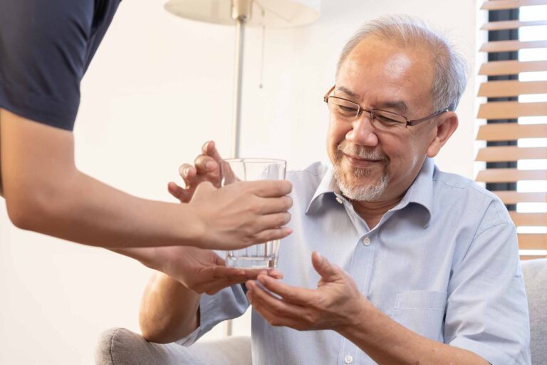 Carer handing an elderly man a glass of water