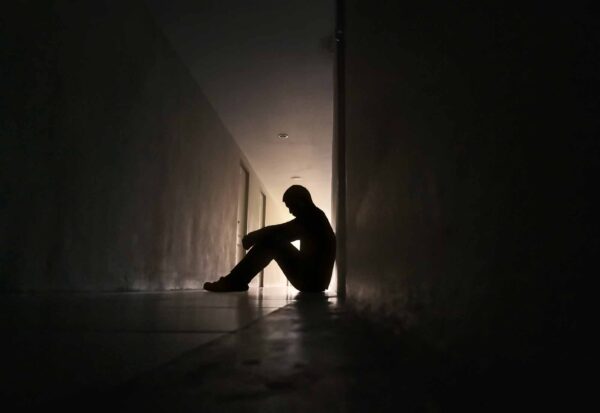Silhouette of a sad man sitting on walkway of residence building.