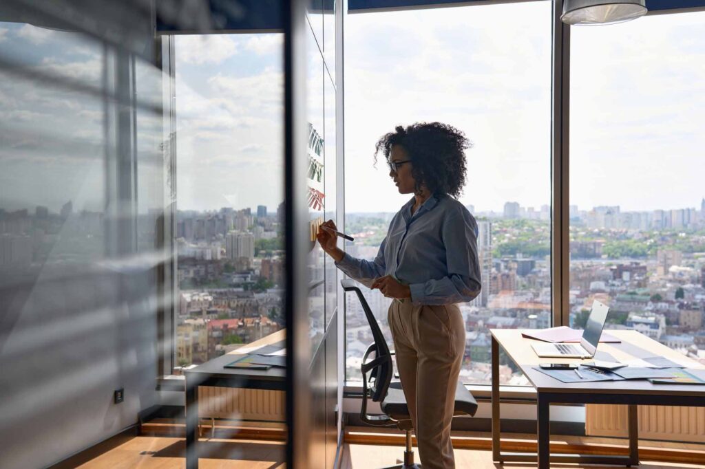 woman writing strategy ideas on sticky notes on whiteboard