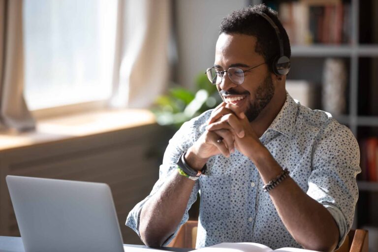 Man in glasses wearing headphones looking at his laptop screen