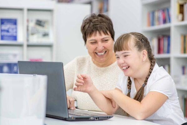 Smiling girl with down syndrome using a laptop with a woman
