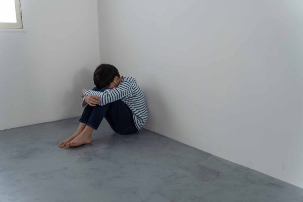 A,Boy,Crouching,In,The,Corner,Of,A,Dark,Room.