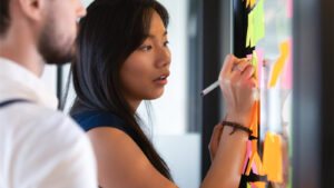 Woman writing idea or task on post it sticky notes on glass wall