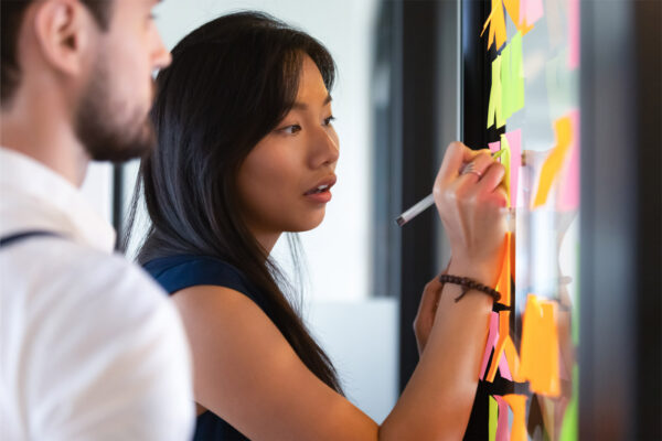 Woman writing idea or task on post it sticky notes on glass wall