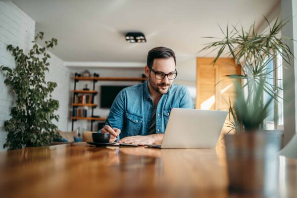 man taking notes and looking at laptop