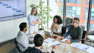 Senior female ceo and multicultural business people discussing company presentation at boardroom table.