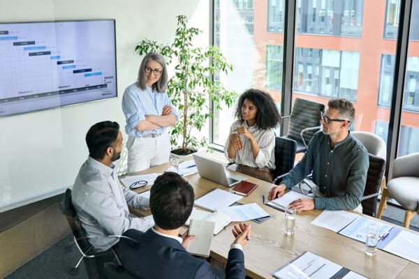 Senior female ceo and multicultural business people discussing company presentation at boardroom table.