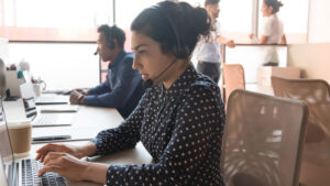 Woman wearing wireless headset working with team using computer.