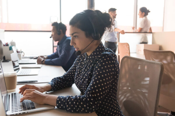 Woman wearing wireless headset working with team using computer.